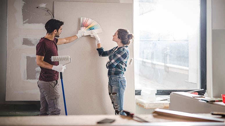 Male and female couple comparing paint charts against a blank wall